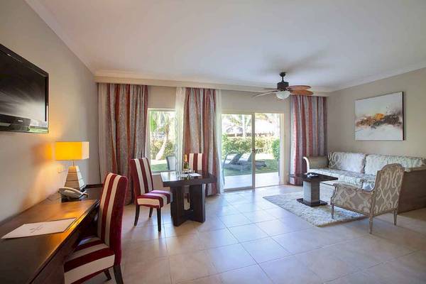 Innenraum des Majestic Elegance Punta Cana Hotels mit Schreibtisch, Stühlen, Tisch, Couch, Fernseher und offener Terrasse.