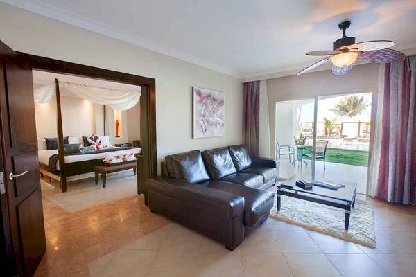 Innenansicht einer Suite im Majestic Elegance Punta Cana mit Doppelbett, Sofa und offenem Fenster.