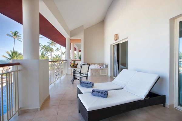 Balkon des Majestic Elegance Punta Cana Hotels mit zwei Sonnenliegen und Blick auf den Pool und Palmen.
