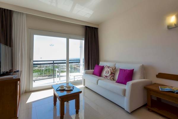 Wohnzimmer mit weißem Sofa, Tisch, Fernseher und Terrassenblick auf das Meer.