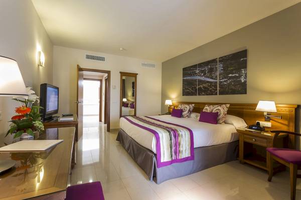 Hotelzimmer im Grand Palladium Palace Ibiza Resort & Spa mit Fernseher, Blumen und bequemem Bett.