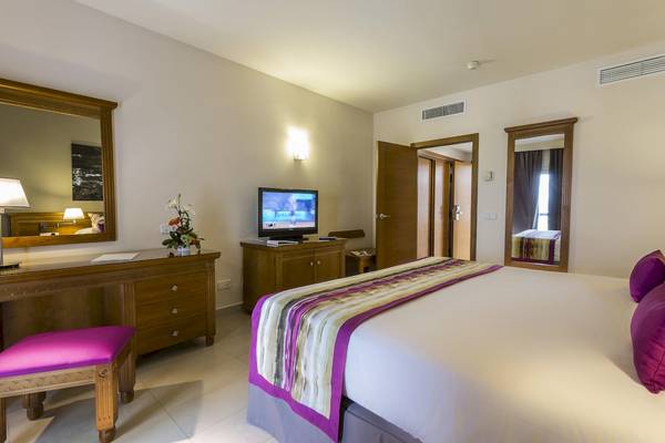 Innenansicht eines Hotelzimmers im Grand Palladium Palace Ibiza Resort & Spa mit Bett, Fernseher und Schreibtisch.
