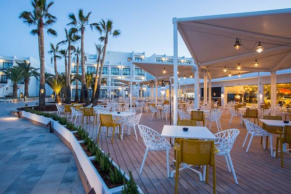 Terrasse im Grand Palladium Palace Ibiza Resort & Spa mit weißen Tischen und Stühlen, abendlicher Beleuchtung und Palmen.