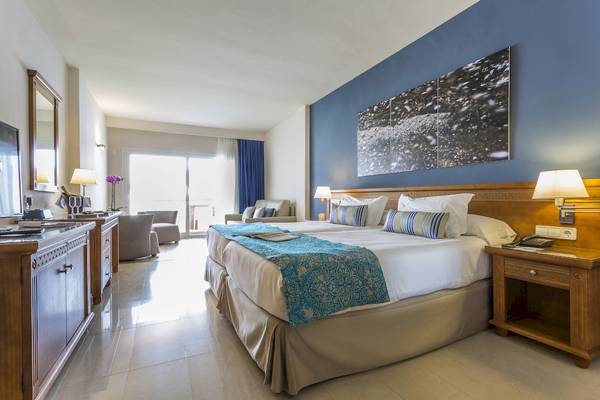 Schlafzimmer im Grand Palladium Palace Ibiza Resort & Spa mit zwei Betten, Nachttischen und Panoramafenstern.