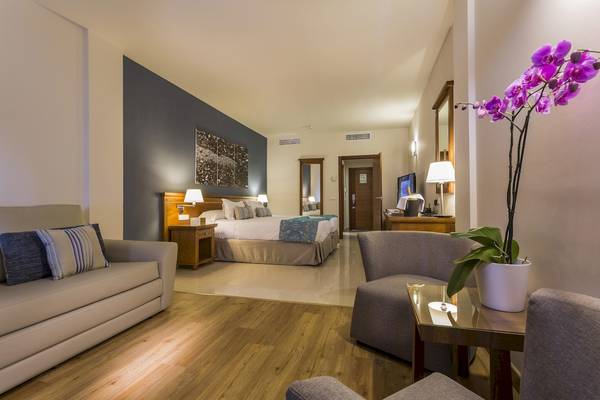 Suite-Schlafzimmer im Grand Palladium Palace Ibiza Resort mit Bett, Sofa und Fernseher.