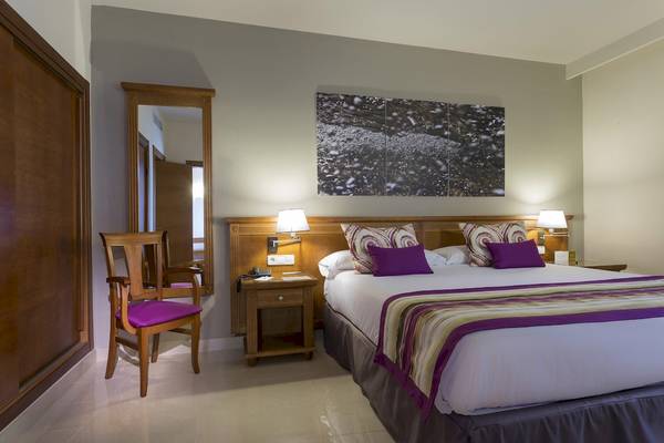 Schlafzimmer im Grand Palladium Palace Ibiza Resort & Spa mit einem Doppelbett, Nachttischen, Lampen und einem Spiegel.