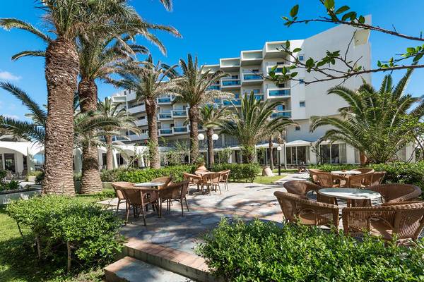Außenbereich des Apollo Beach Hotels mit Palmen, Tischen und Stühlen vor einem modernen Gebäude.