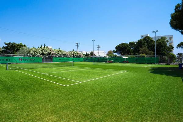 Tennisplatz auf dem Apollo Beach Hotelgelände, mit einem geschlossenen Schirm und grünem Rasen.