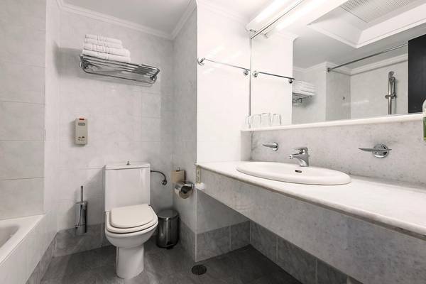 Badezimmer im Apollo Beach Hotel mit weißer Fliesenwand, Toilette, Waschbecken und Spiegel.