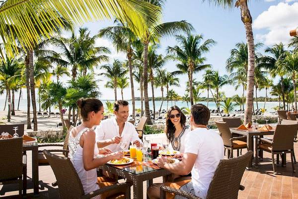 Vier Personen sitzen an einem Tisch auf der Terrasse des Barcelo Maya Grand Resort und essen.