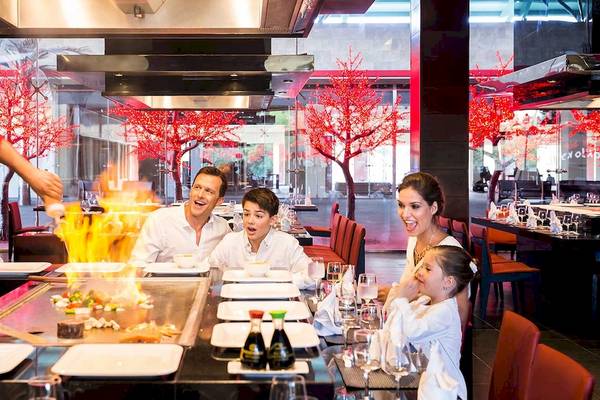 Familie genießt ein Essen in einem Restaurant im Barcelo Maya Grand Resort mit einem Koch, der eine Flamme am Tisch entfacht.