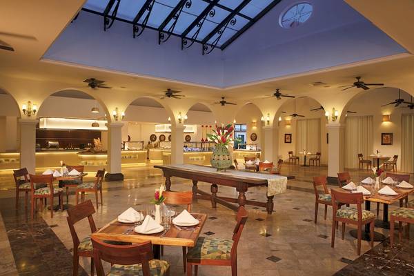 Innenbereich des Restaurants im Dreams Tulum Resort & Spa mit geometrischen Mustern, Holztischen und hängenden Ventilatoren.