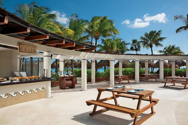 Terrasse des Barefoot Grill im Dreams Tulum Resort & Spa mit holzigen Bänken und Tischen, umgeben von Palmen und Blick auf den Ozean.
