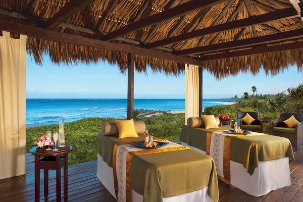 Behandelzimmer mit Meerblick im Dreams Tulum Resort & Spa mit zwei Massageliegen und einem Tisch mit Getränken.