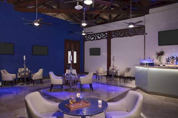 Loungebereich im Dreams Tulum Resort & Spa mit blauen Wänden, weißen Sesseln und einem Tresen mit Getränken.