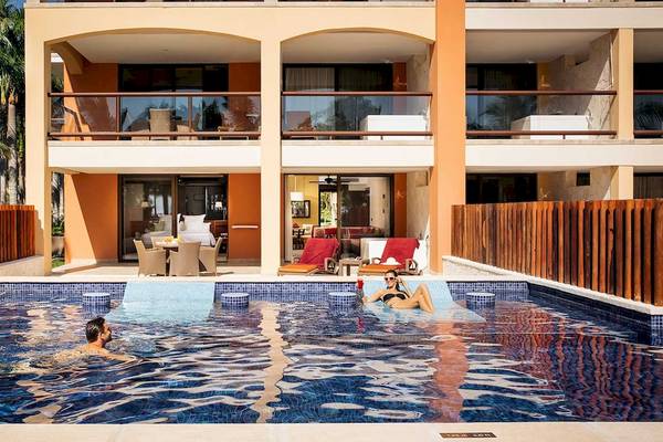 Zwei Personen schwimmen im Swimmingpool des Barcelo Maya Grand Resort, umgeben von Palmen und Möbeln.