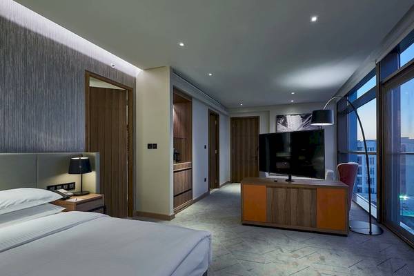 Schlafzimmer im Mysk Al Mouj Hotel mit großem Bett, Fernseher und Fenstern.
