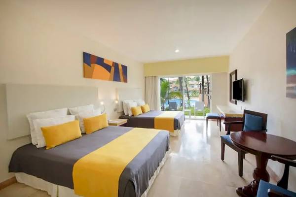 Zimmeransicht im Viva Azteca by Wyndham Hotel mit zwei Betten, gelben Kissen und Fernseher an der Wand.