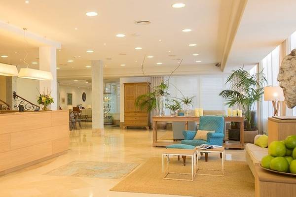 Rezeption im Universal Hotel Neptuno mit hellem Interieur, Holzmöbeln und Pflanzen.