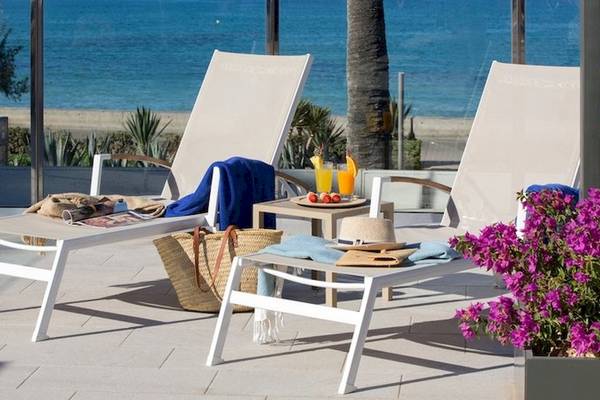 Zwei weiße Liegen auf der Terrasse des Universal Hotel Neptuno mit Meerblick, Getränken und Blumen.