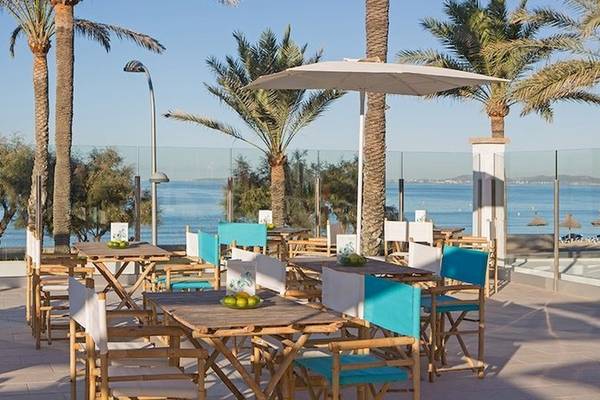 Außenterrasse des Universal Hotel Neptuno mit blauen Stühlen, Tischen und Sonnenschirmen mit Blick auf das Meer.