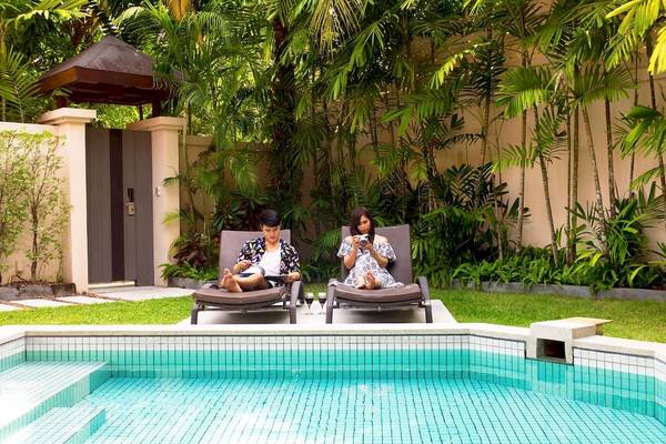 Zwei Gäste entspannen auf Loungestühlen neben dem Pool im Dewa Phuket Resort & Villas.