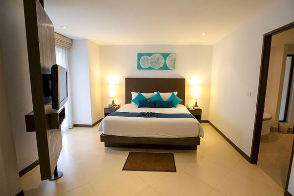 Schlafzimmer im Dewa Phuket Resort & Villas mit einem Bett, Kissen, Lampe und Fernseher.