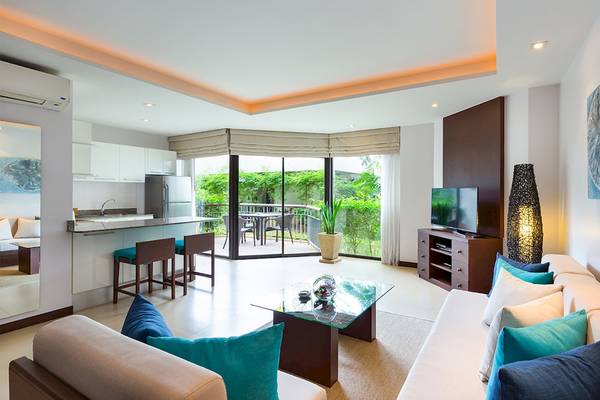 Innenansicht des Wohnzimmers im Dewa Phuket Resort & Villas mit offener Küche, Balkon und Fernseher.