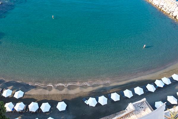Luftaufnahme des Royal Apollonia Strandes mit vielen weißen Sonnenschirmen und zwei Personen im Wasser.