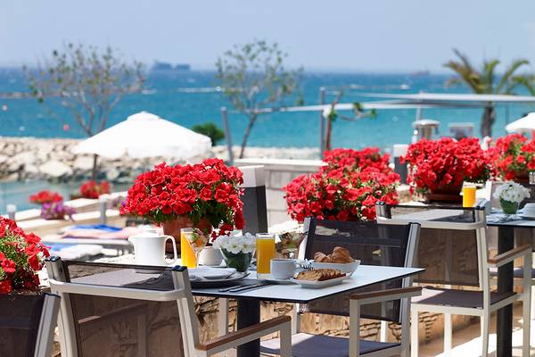Frühstückstisch mit Meerblick im Royal Apollonia Beach Hotel mit roten Blumen und Meereshintergrund