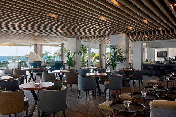 Innenbereich des Royal Apollonia Beach Hotels mit Tischen, Stühlen und Blick auf das Meer.