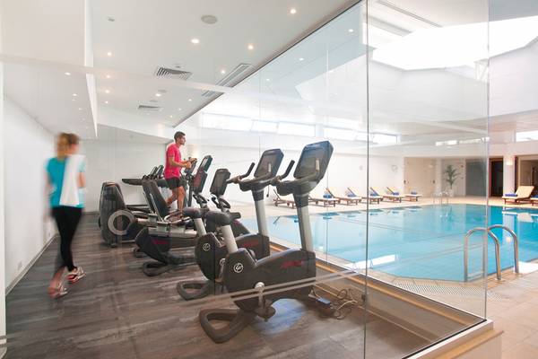 Fitnesszentrum im Royal Apollonia Beach Hotel mit einer Person auf einem Laufband und einer Frau, die läuft.