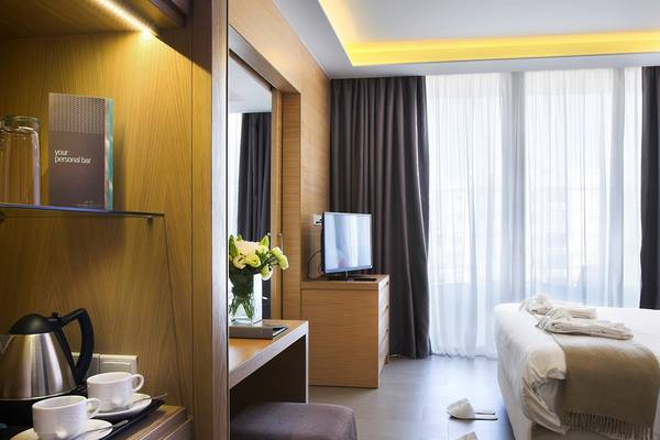 Innenansicht eines Zimmers im Royal Apollonia Beach Hotel mit Bett, Schreibtisch und Fernseher.