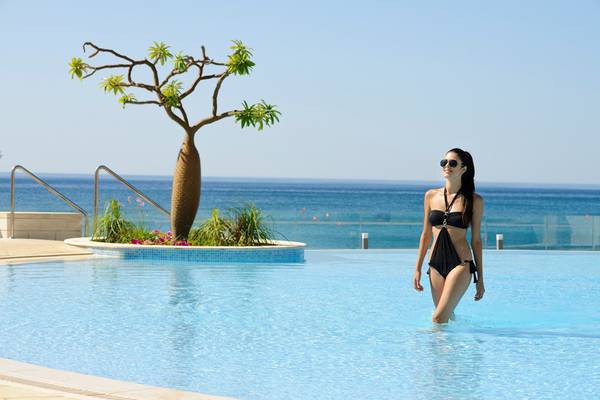 Eine Frau in einem schwarzen Bikini geht durch das Schwimmbad des Royal Apollonia Beach Hotels.