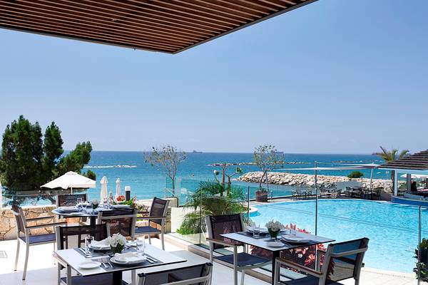 Außenbereich des Apollonia Beach Hotel mit Tischen und Stühlen und Blick auf den Pool und das Meer.