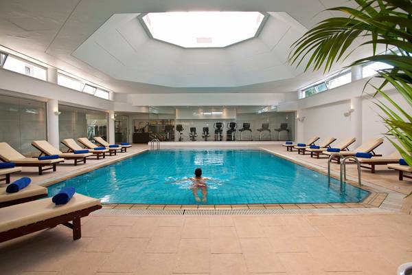 Ein Schwimmer im Innenpool des Royal Apollonia Beach Hotels, umgeben von Liegestühlen und Fitnessgeräten.