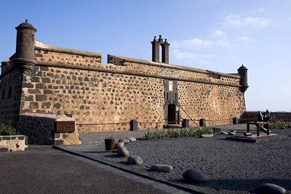 Außenansicht des Seaside Los Jameos Hotels mit einer steinernen Mauer, Tür und zwei Türmen.