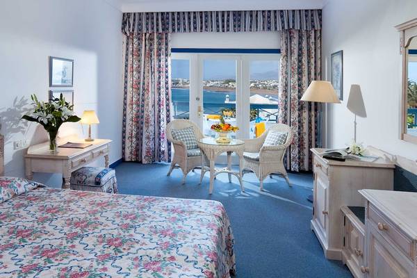 Zimmer im Seaside Los Jameos Hotel mit Meerblick, Blumenvase, Schreibtisch und zwei Rattanstühlen.