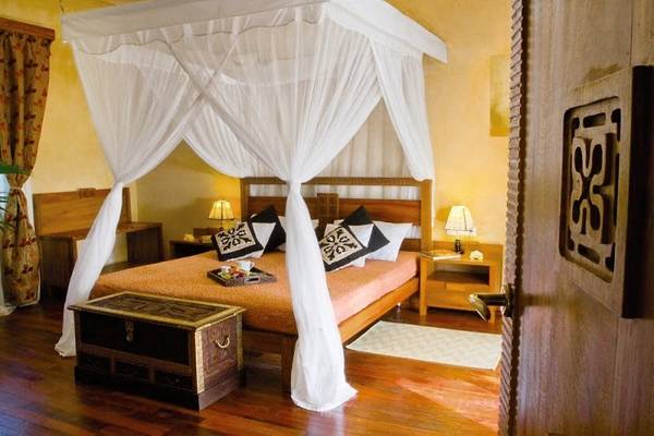 Ein luxuriöses Bettzimmer im Zanzi Resort mit einem Baldachin, einem Holzbett und Kissen.