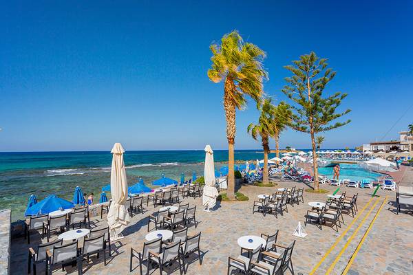 Außenbereich des Olympos Beach Resorts mit Tischen, Stühlen und Sonnenschirmen am Strand.