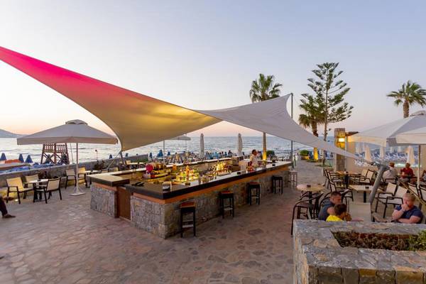 Terrasse des Olympos Beach Resorts mit Blick auf das Meer, mit Gästen an Tischen und Sonnenschirmen.