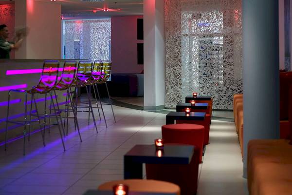 Lobby-Bar im Radisson Blu Resort Split mit lila Beleuchtung, roten Hockern und weißen Trennwänden.