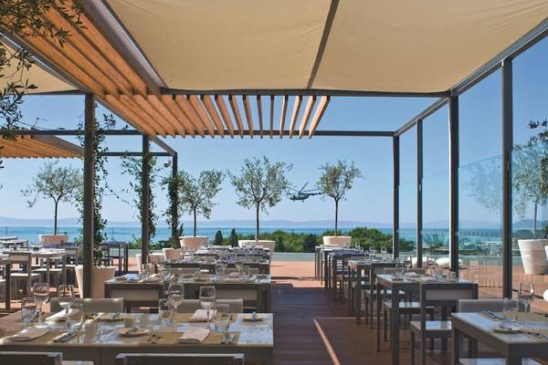 Außenbereich des Radisson Blu Resort Split mit Tischen und Stühlen am Meer.