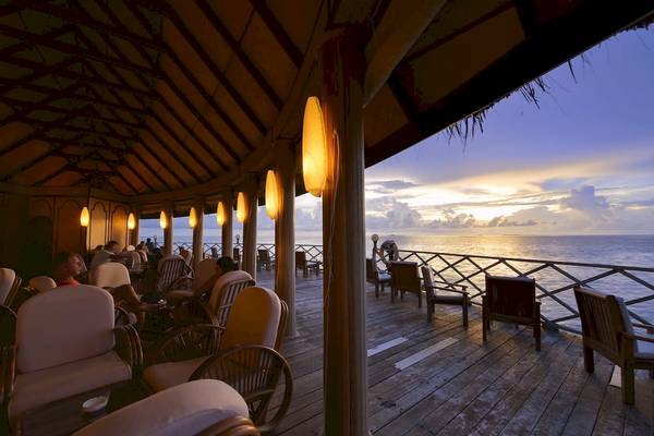 Terrasse des Angaga Island Resort & Spa mit Blick auf den Sonnenuntergang über dem Meer.