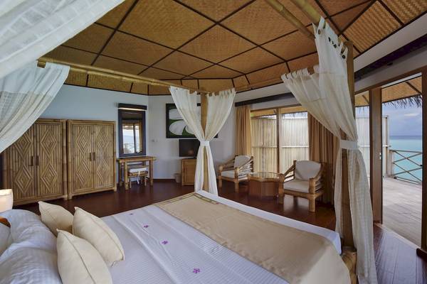 Innenansicht einer Suite im Angaga Island Resort & Spa mit einem großen Bett, weißen Vorhängen und Blick auf das Meer.