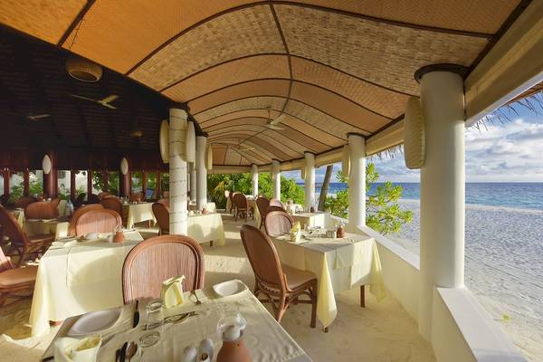 Außenbereich eines Restaurants im Angaga Island Resort & Spa mit Tischen und Stühlen am Strand.