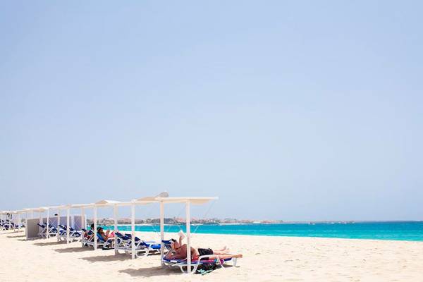 Personen entspannen auf Sonnenliegen am Strand des Dunas De Sal Hotels.