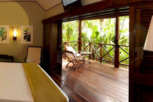 Innenansicht eines Hotelzimmers im Paradise Sun Hotel mit einem großen Bett, einem Balkon und einer Aussicht auf den Dschungel.