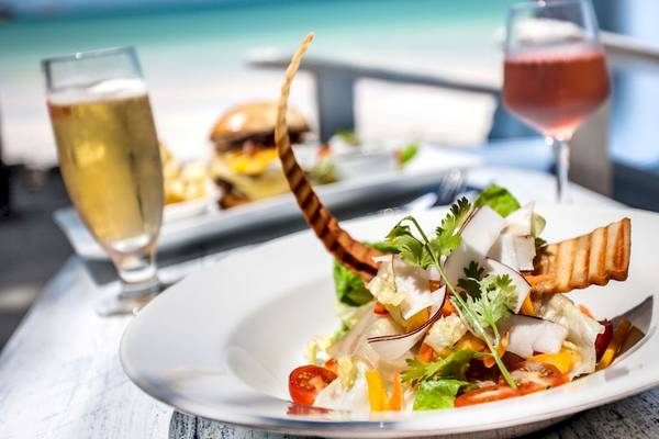 Ein Teller mit Salat und anderen Gerichten auf einem Tisch am Strand mit Getränken und einer schönen Aussicht.