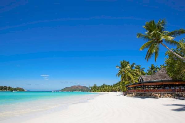 Strand mit weißem Sand und blauem Wasser, Palmen und Restaurant am Paradise Sun Hotel